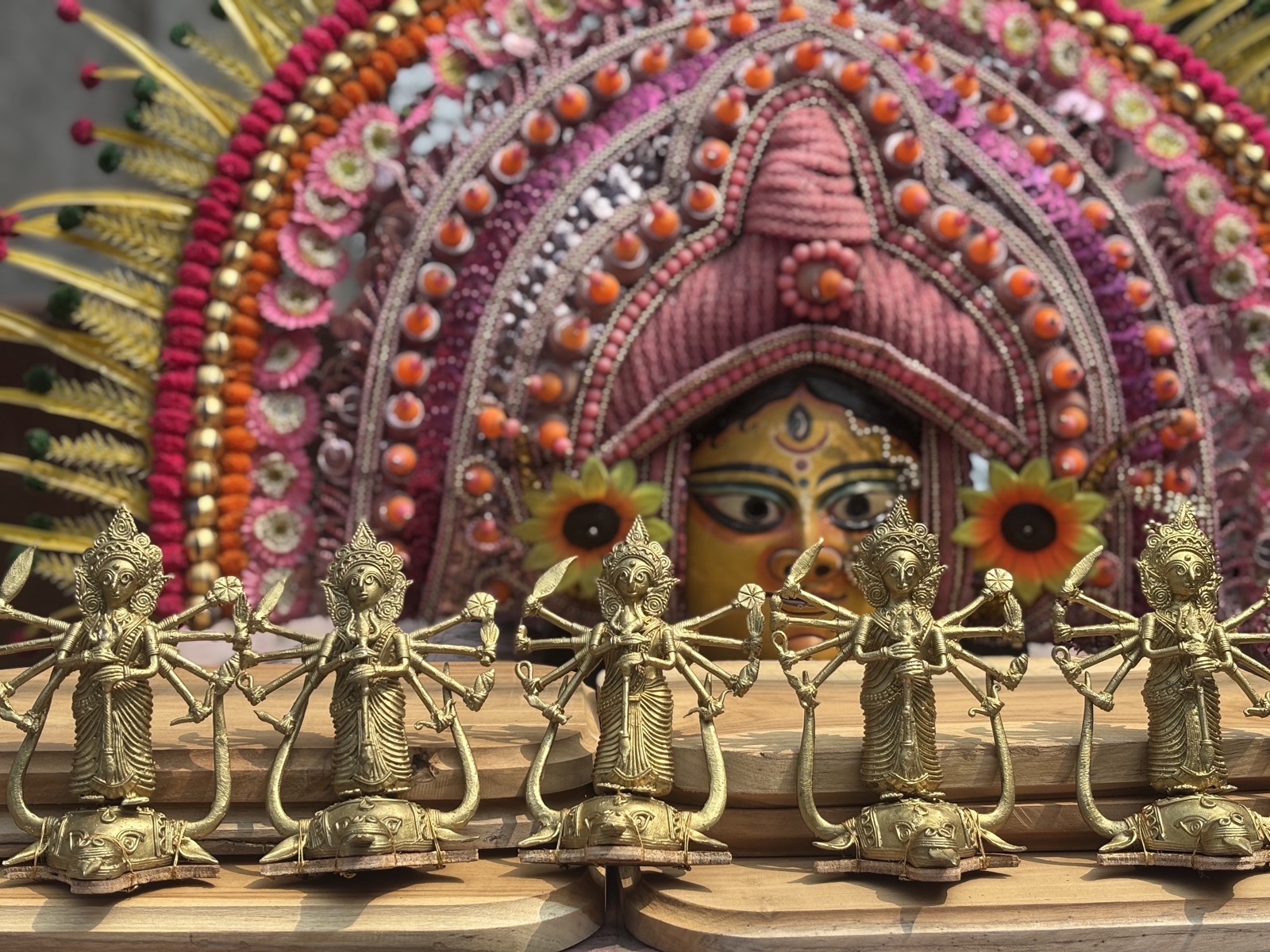 A row of brass Dokra Durga figures for the awards, in front of a Chhau mask of Durga