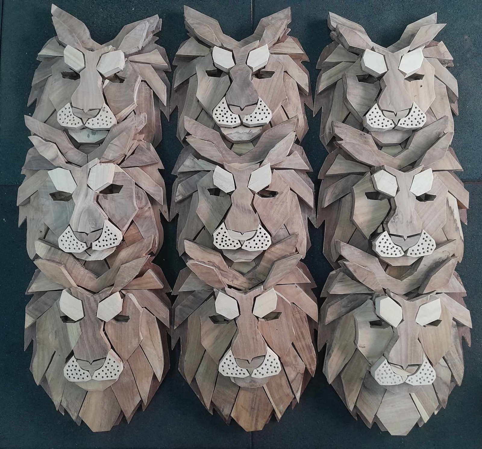 Nine wooden lion faces made of layered wood pieces, laid out in the workshop